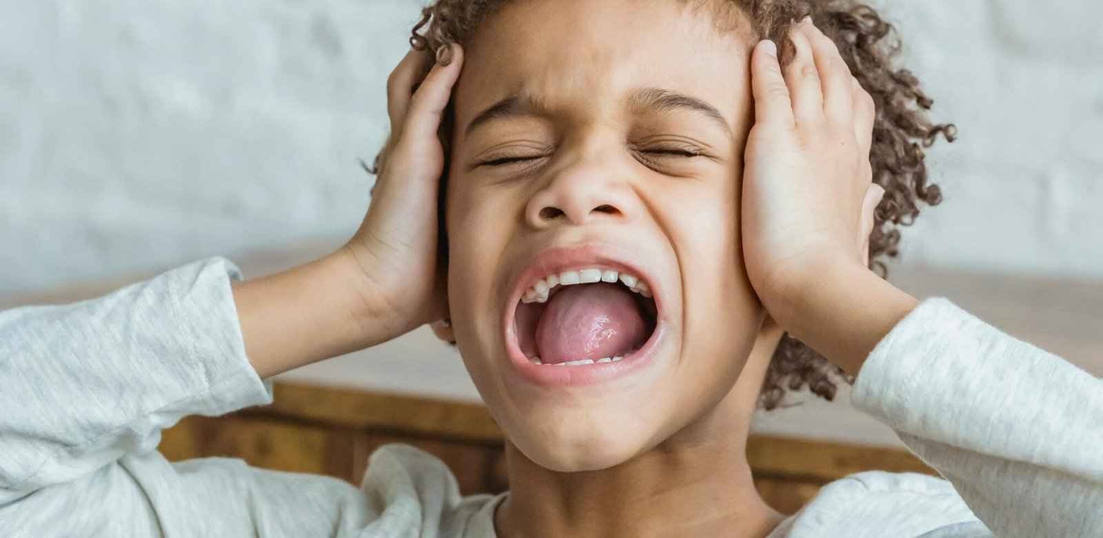 Desperate African American boy with curly hair in casual wear touching head while shouting in light room at home near wall