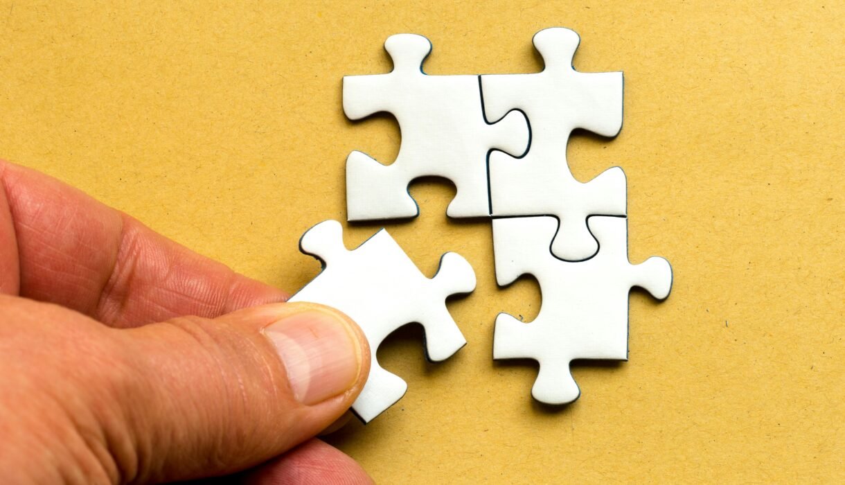 Close-up of a hand completing a white jigsaw puzzle on a yellow background.