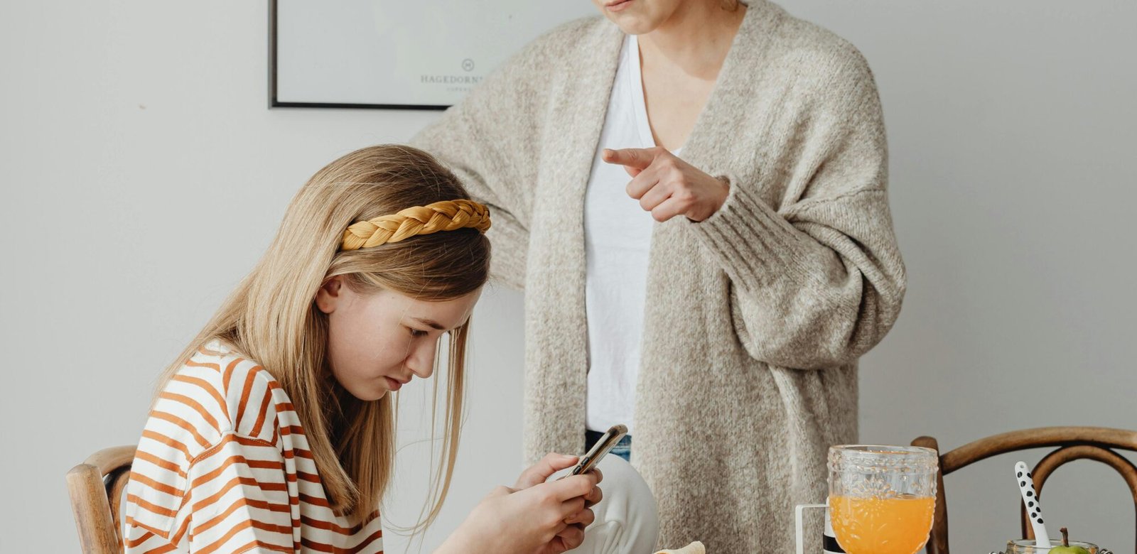 A mother and daughter in a serious conversation at the dining table with a smartphone in focus.
